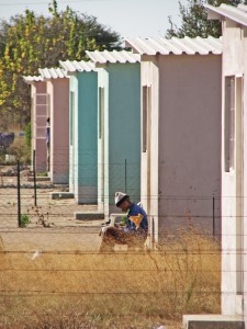 Figure 5. Young man sits outside row of concrete houses in center of Tsumkwe, Namibia.
